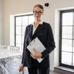 Confident real estate agent standing indoors holding property documents.